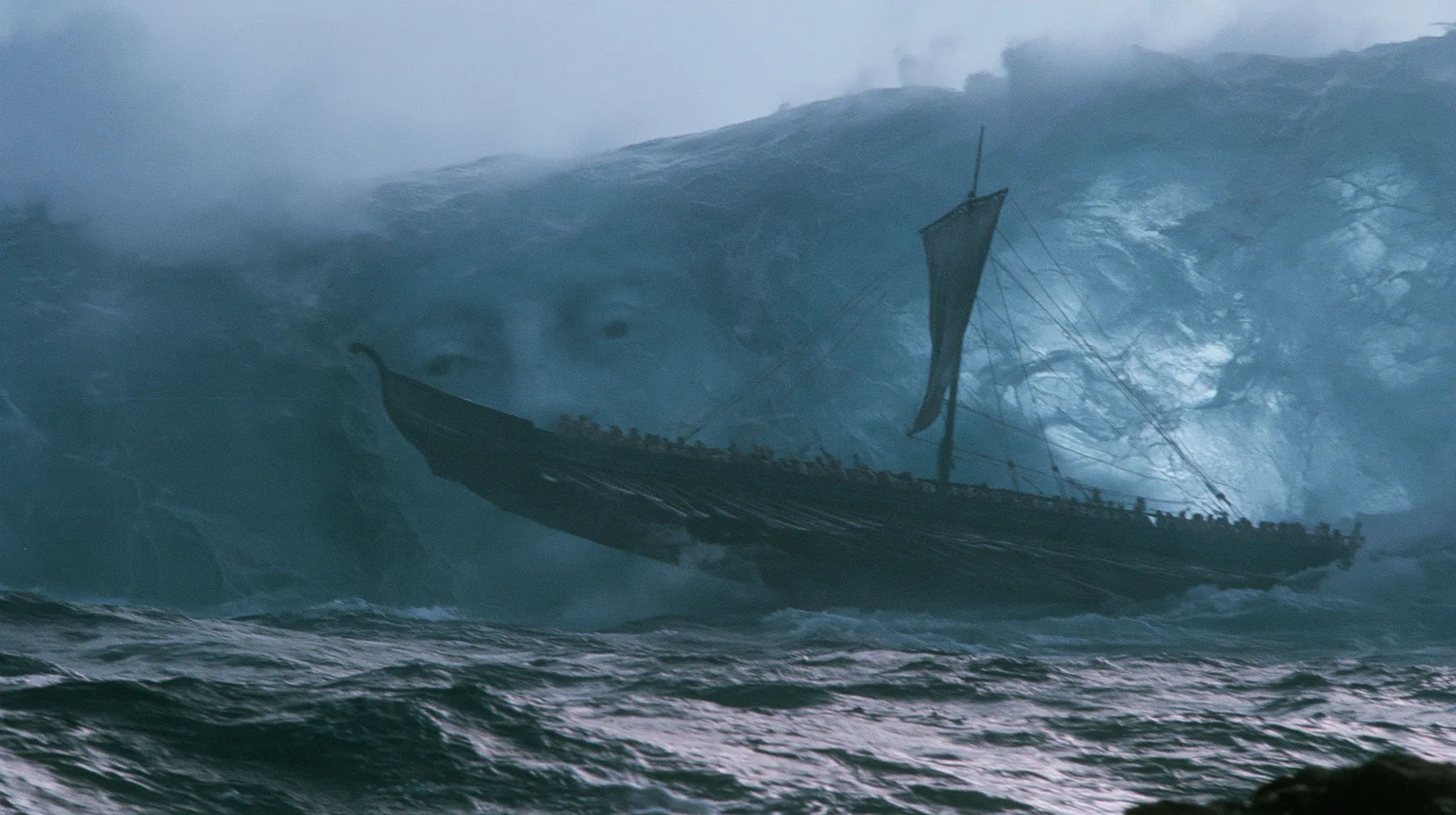 wide shot of a long black ancient Greek galley with a single mast, a square sail and two banks of oars lifted high on a rising mountain of water, and through the translucent face of the swell a colossal pale woman's…