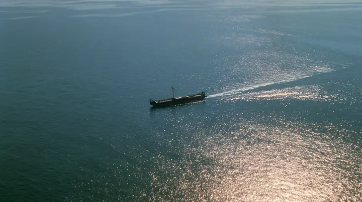extreme high aerial of a long black ancient Greek galley with a single mast, a square sail and two banks of oars as a tiny dark shape on a vast sparkling morning sea, its wake a thin white line, clear morning light…