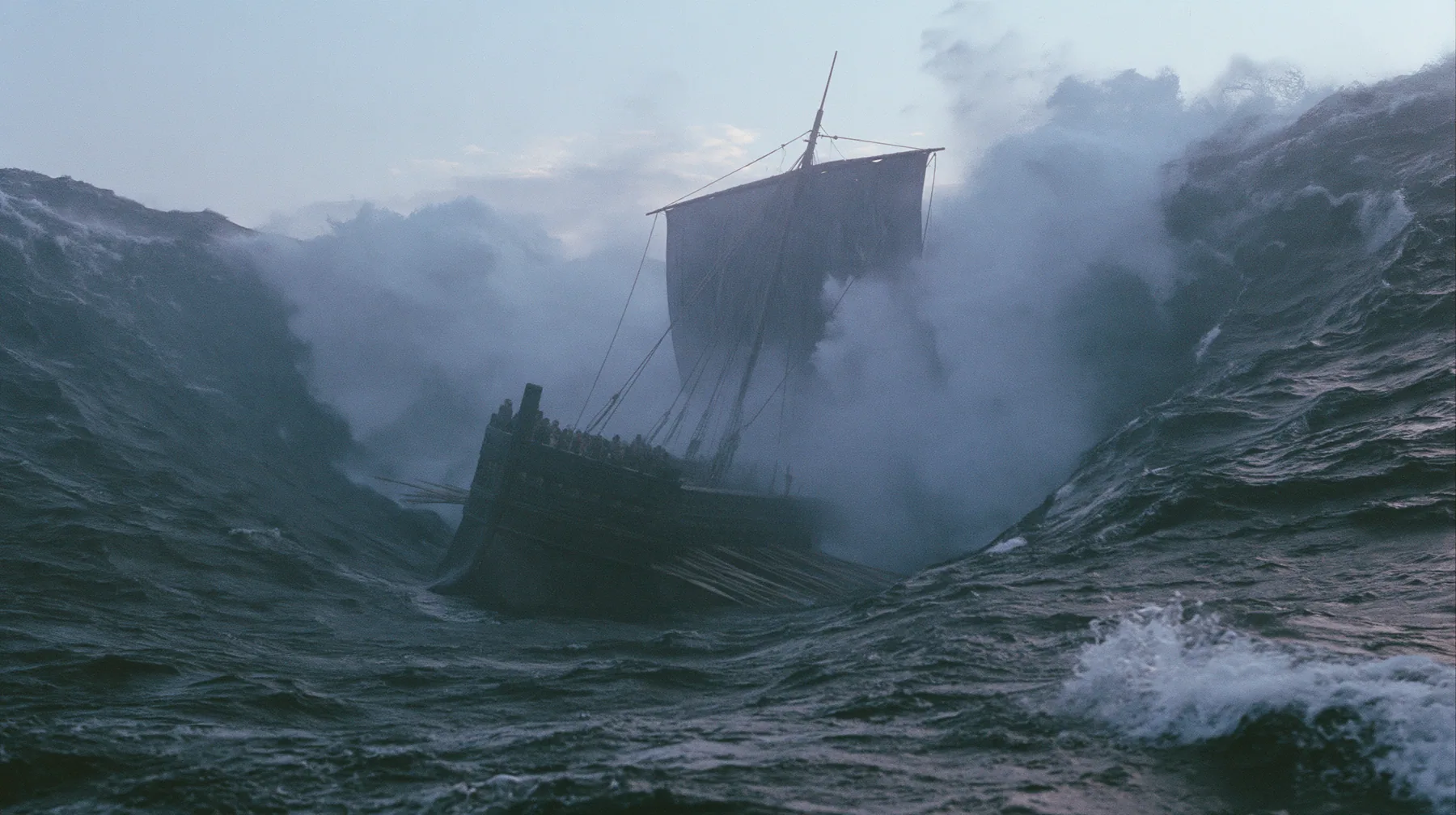 wide shot of a long black ancient Greek galley with a single mast, a square sail and two banks of oars dropping into an enormous trough as the sea falls away around it, walls of dark water on both sides, grey first…