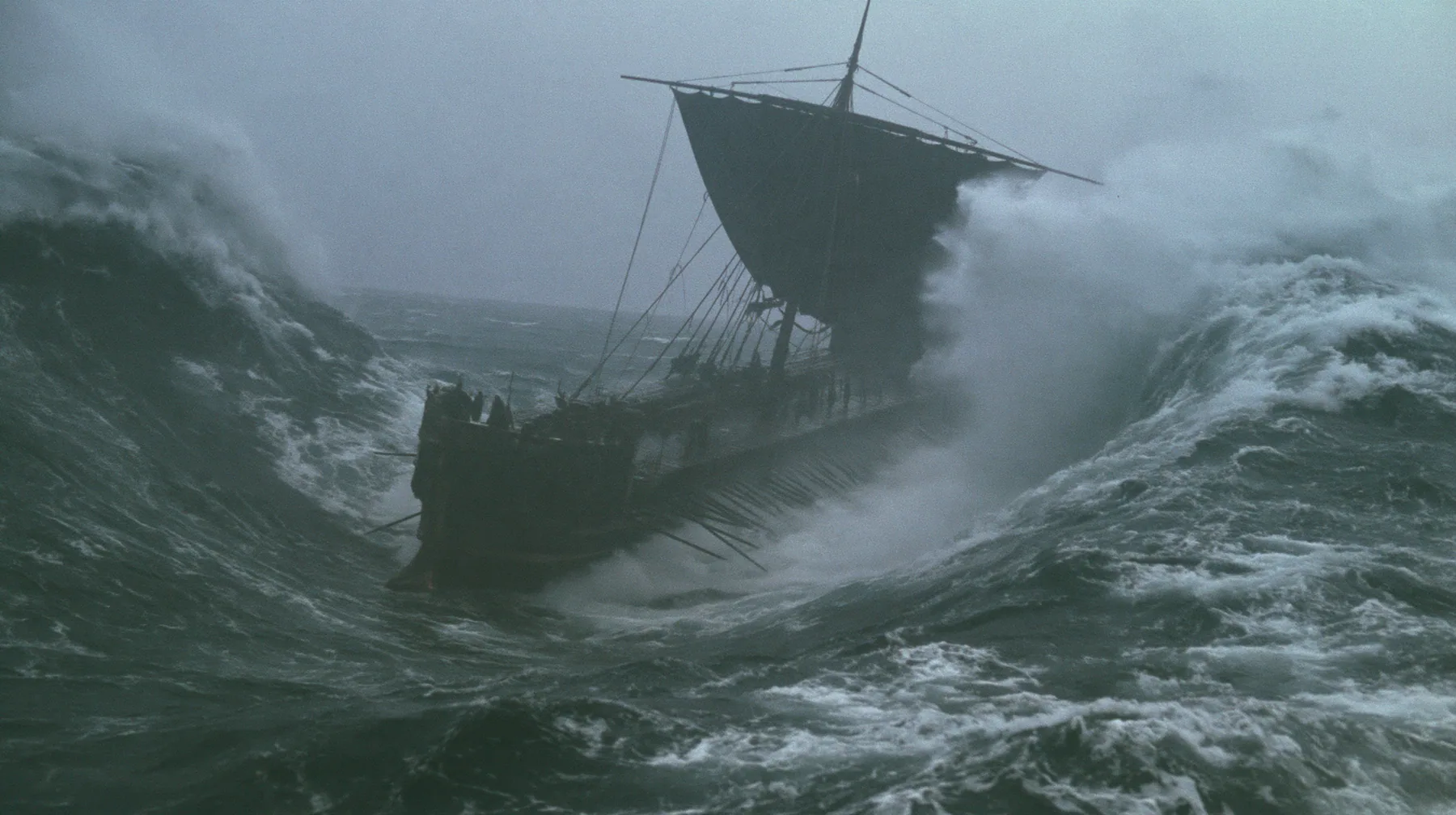 wide shot of a long black ancient Greek galley with a single mast, a square sail and two banks of oars dropping into an enormous trough as the sea falls away around it, walls of dark water on both sides, grey first…