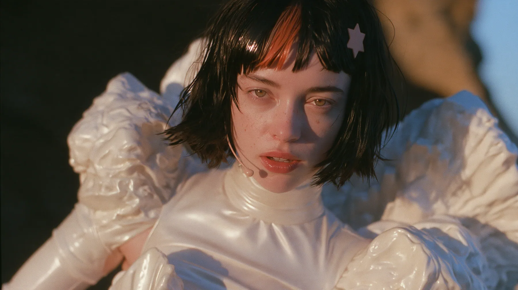 medium shot of a Caucasian American woman in her mid-twenties with pale skin and light freckles, a glossy black blunt jaw-length bob with heavy straight bangs and one clay-orange streak through the bangs, a small…