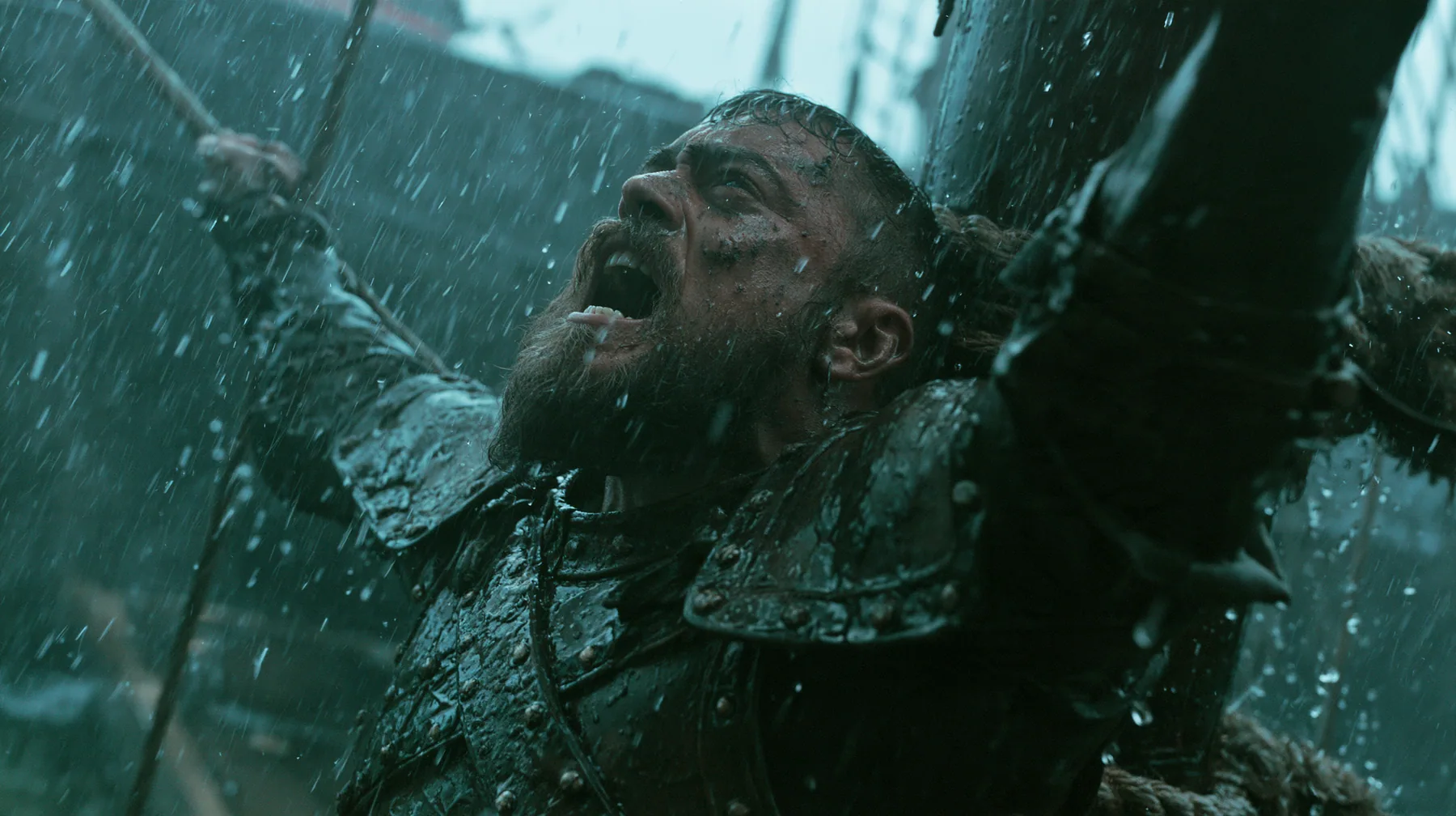 a bearded man in battered leather armour lashed to the mast of a black ship in a storm, screaming at the sky, large-format film still, practical storm, rain and spray, teal and black, no text, no letters, no logos