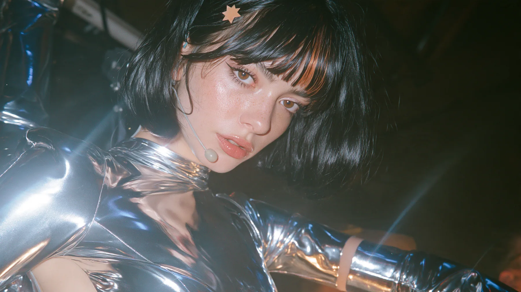 full-length fashion photograph from head to toe of a Caucasian American woman in her mid-twenties with pale skin and light freckles, a glossy black blunt jaw-length bob with heavy straight bangs and one clay-orange…
