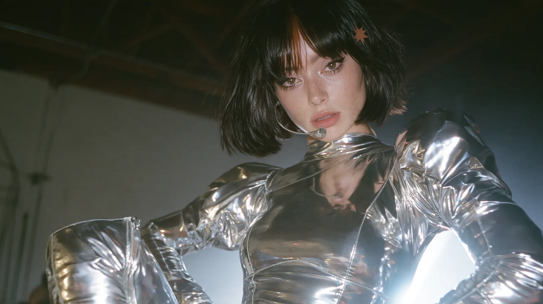 full-length fashion photograph from head to toe of a Caucasian American woman in her mid-twenties with pale skin and light freckles, a glossy black blunt jaw-length bob with heavy straight bangs and one clay-orange…