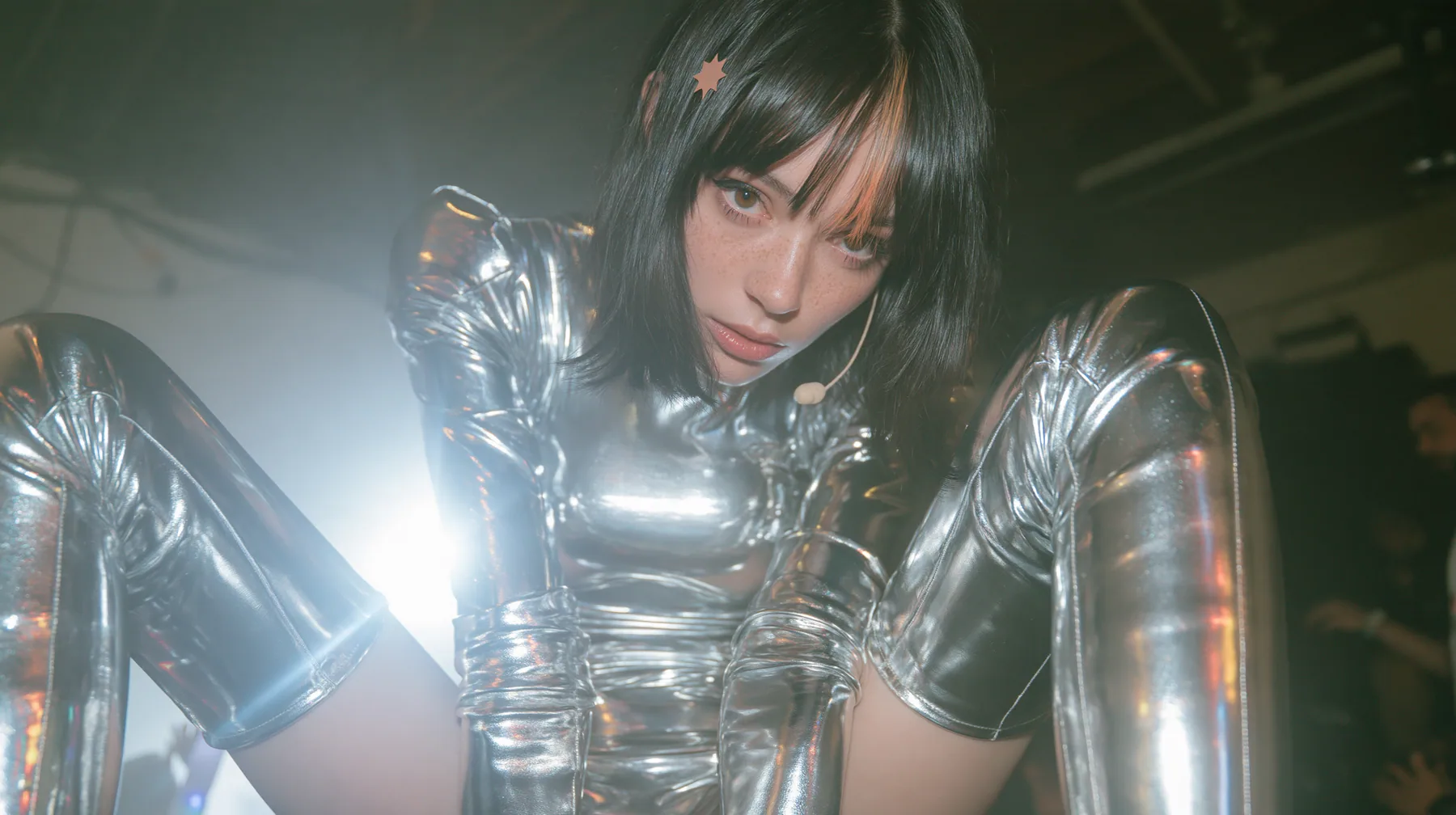 full-length fashion photograph from head to toe of a Caucasian American woman in her mid-twenties with pale skin and light freckles, a glossy black blunt jaw-length bob with heavy straight bangs and one clay-orange…
