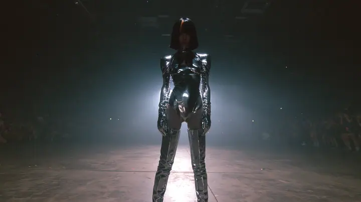 extreme wide shot of a vast dark warehouse rave, and alone in the middle of the empty concrete floor a young Caucasian American woman with pale skin, a glossy black blunt jaw-length bob with heavy straight bangs and…