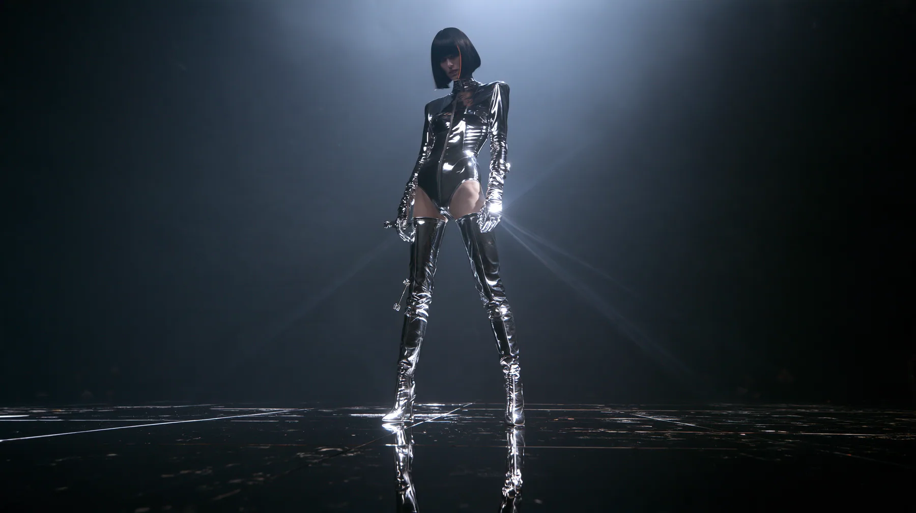 full-body fashion editorial photograph taken from far away with a long lens: a young Caucasian American woman with pale skin and a glossy black blunt bob with heavy straight bangs and one clay-orange streak, in a…