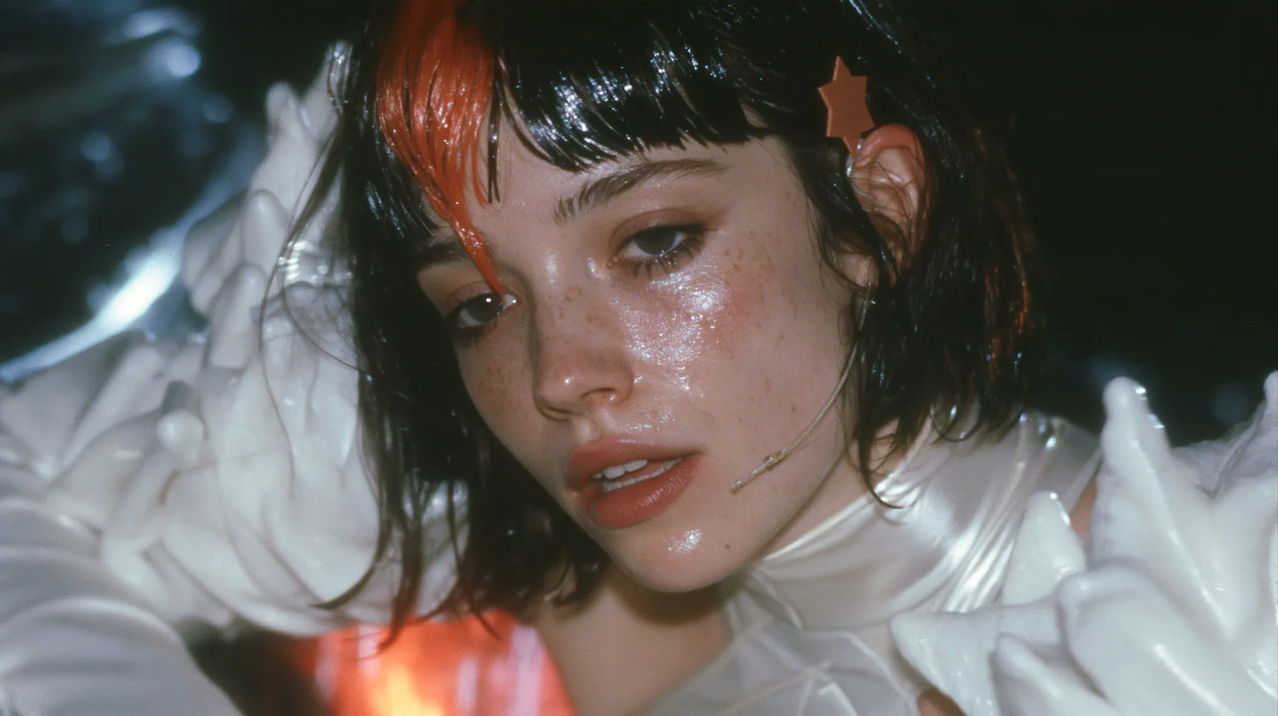 medium close-up of a Caucasian American woman in her mid-twenties with pale skin and light freckles, a glossy black blunt jaw-length bob with heavy straight bangs and one clay-orange streak through the bangs, a small…