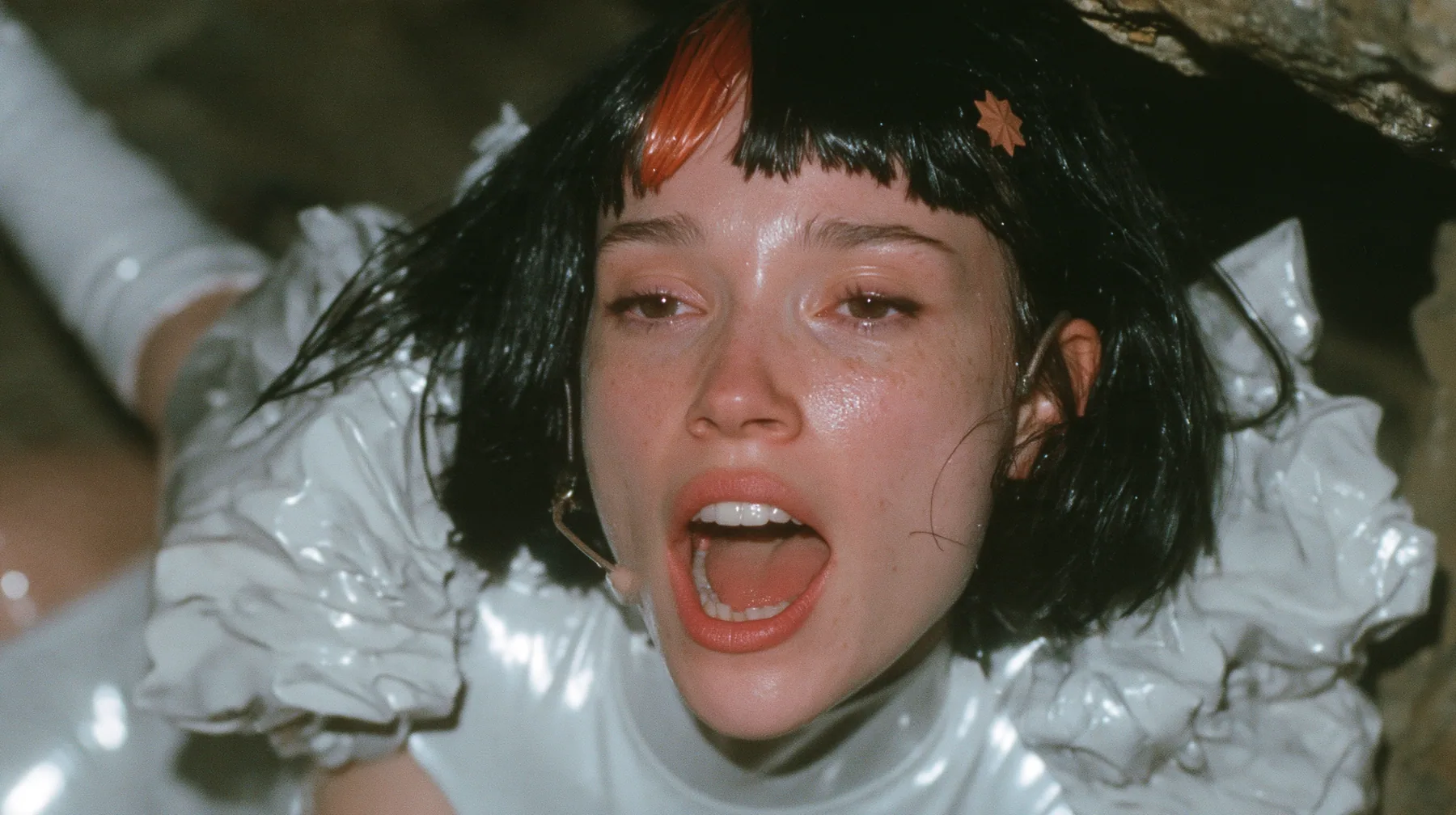 medium close-up of a Caucasian American woman in her mid-twenties with pale skin and light freckles, a glossy black blunt jaw-length bob with heavy straight bangs and one clay-orange streak through the bangs, a small…