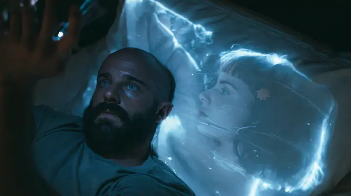 top-down shot of a broad-shouldered Caucasian man in his early thirties with a shaved head, a thick short dark beard, a square jaw, heavy brows and pale blue eyes, the build of a man who lifts, in a grey t-shirt,…