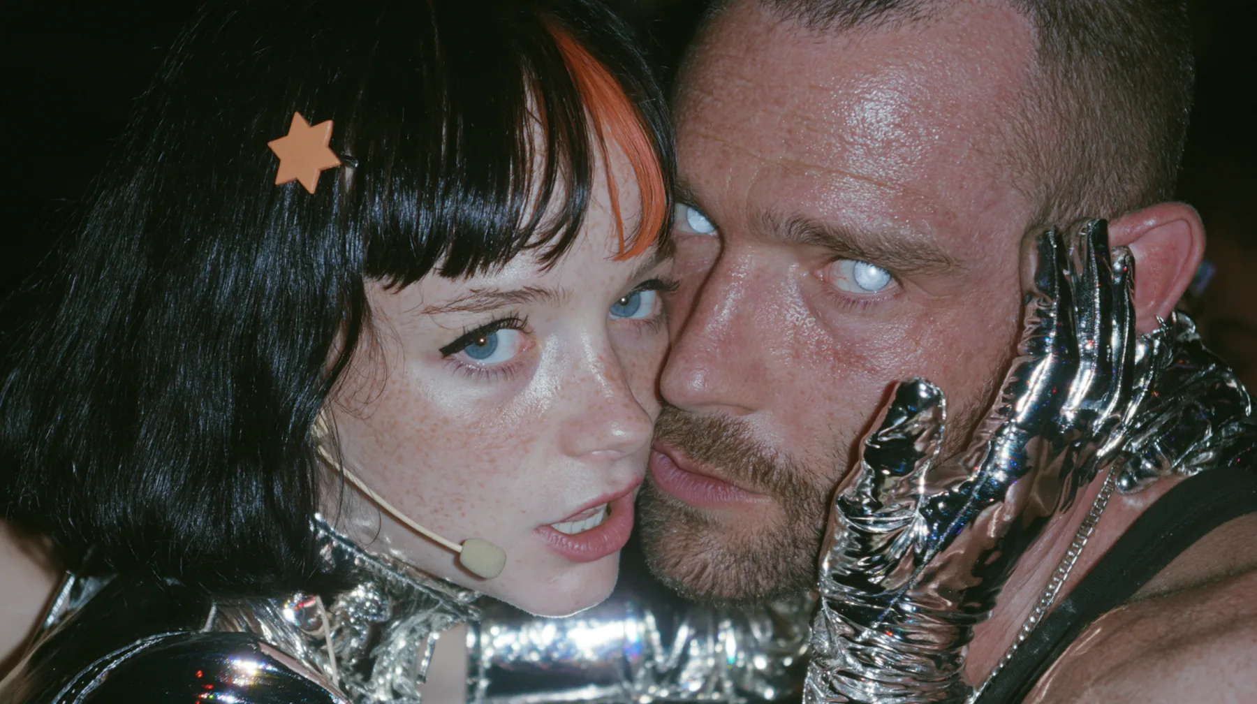 extreme close-up of a Caucasian American woman in her mid-twenties with pale skin and light freckles, a glossy black blunt jaw-length bob with heavy straight bangs and one clay-orange streak through the bangs, a…