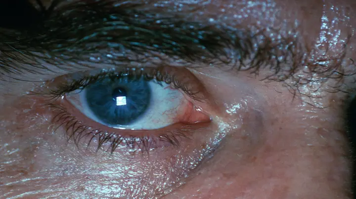 extreme close-up of a man's wide-open pale blue eye at 3am, bloodshot, heavy brow, the glowing rectangle of a phone screen reflected in the eye, a dark bedroom at 3am lit only by a phone screen, blue-white glow on…