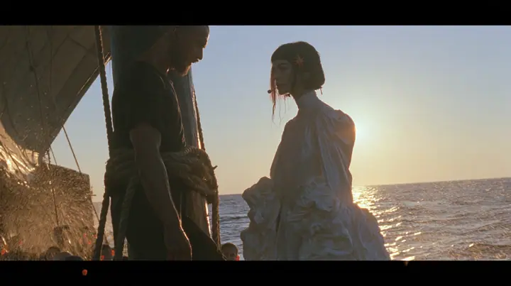 side view at sunrise on the deck of a long black ancient Greek galley with a single mast, a square sail and two banks of oars: a broad-shouldered Caucasian man in his early thirties with a shaved head, a thick short…