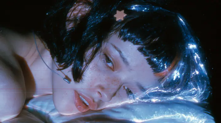 close-up side view of a Caucasian American woman in her mid-twenties with pale skin and light freckles, a glossy black blunt jaw-length bob with heavy straight bangs and one clay-orange streak through the bangs, a…