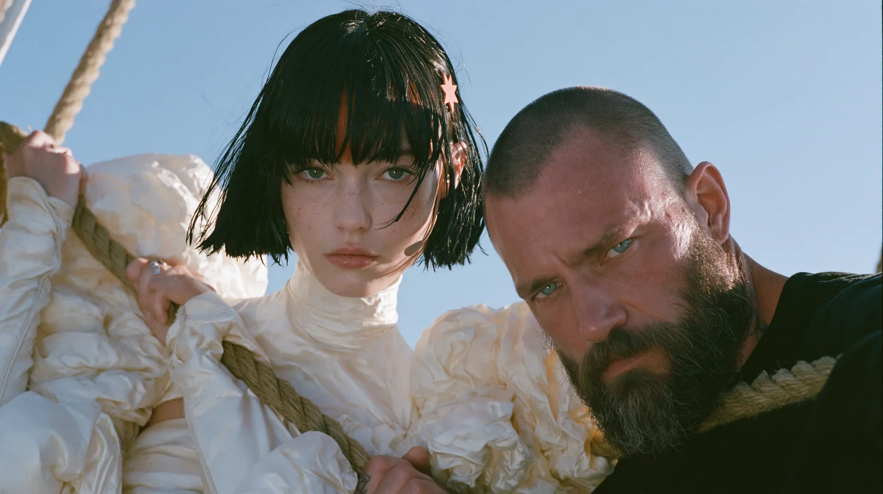 low angle of a Caucasian American woman in her mid-twenties with pale skin and light freckles, a glossy black blunt jaw-length bob with heavy straight bangs and one clay-orange streak through the bangs, a small flat…