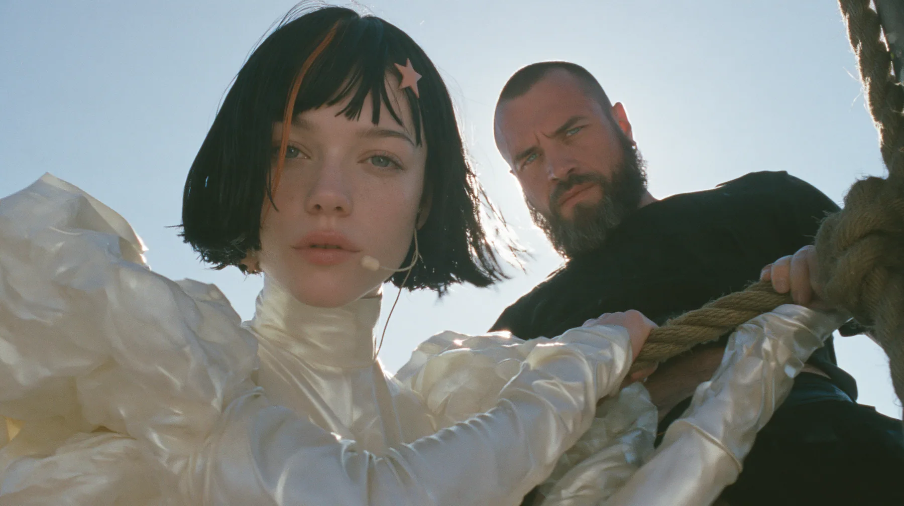 low angle of a Caucasian American woman in her mid-twenties with pale skin and light freckles, a glossy black blunt jaw-length bob with heavy straight bangs and one clay-orange streak through the bangs, a small flat…