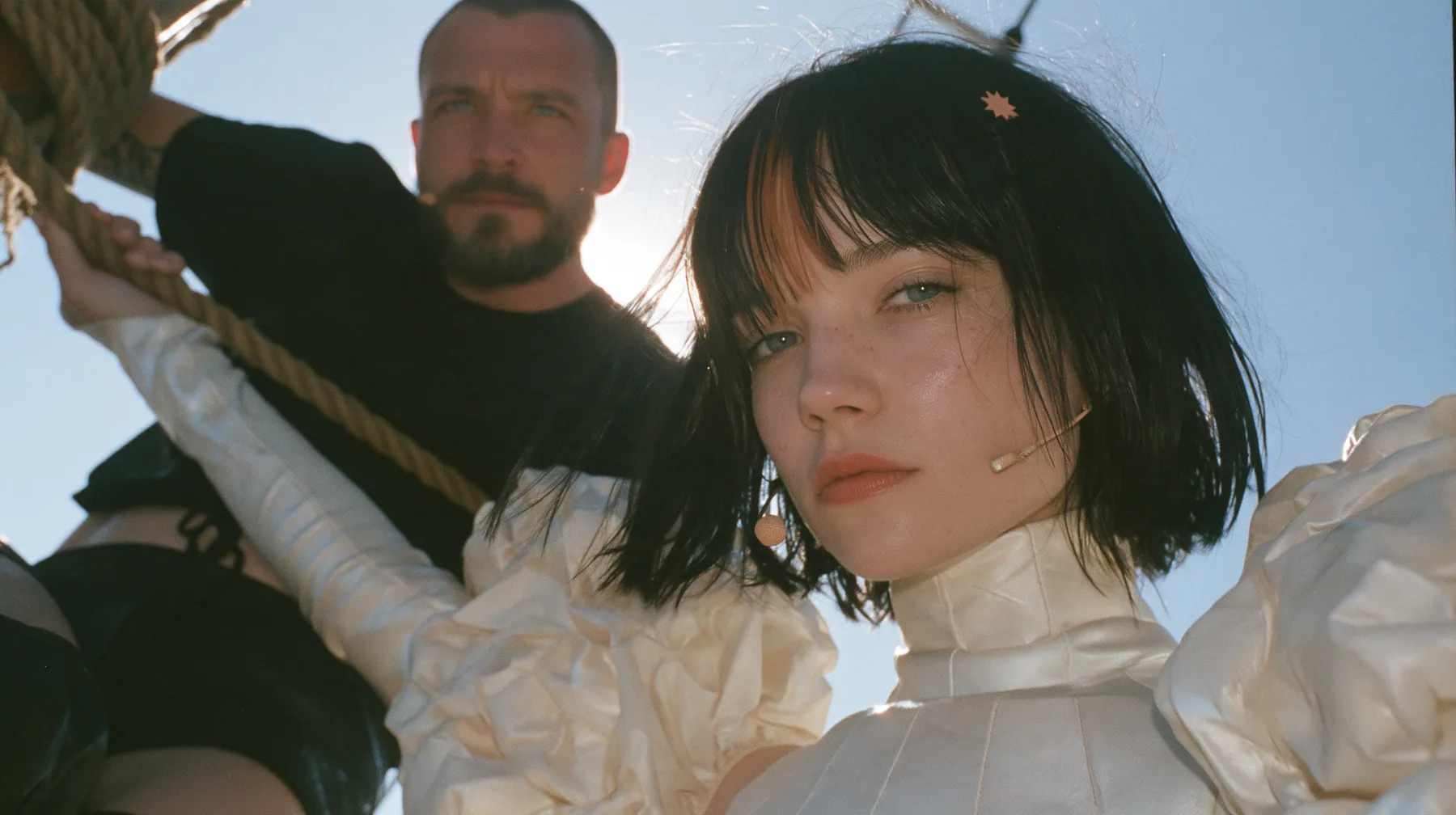 low angle of a Caucasian American woman in her mid-twenties with pale skin and light freckles, a glossy black blunt jaw-length bob with heavy straight bangs and one clay-orange streak through the bangs, a small flat…