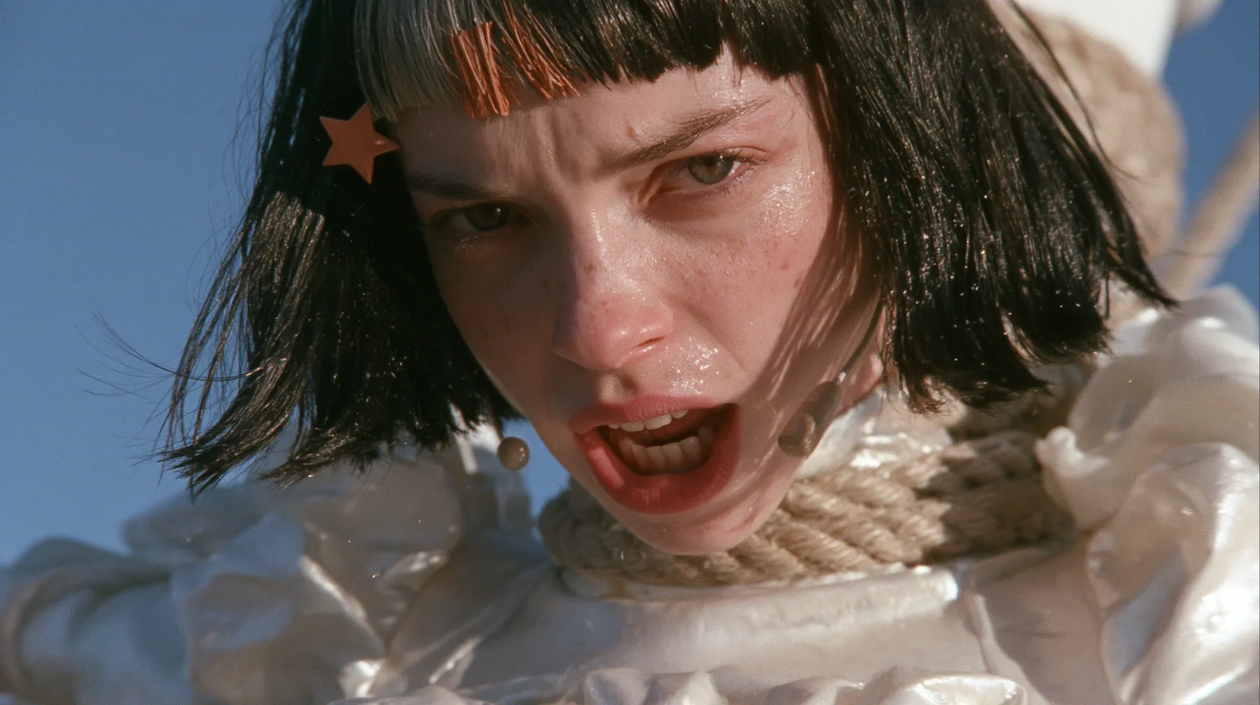 close-up of a Caucasian American woman in her mid-twenties with pale skin and light freckles, a glossy black blunt jaw-length bob with heavy straight bangs and one clay-orange streak through the bangs, a small flat…
