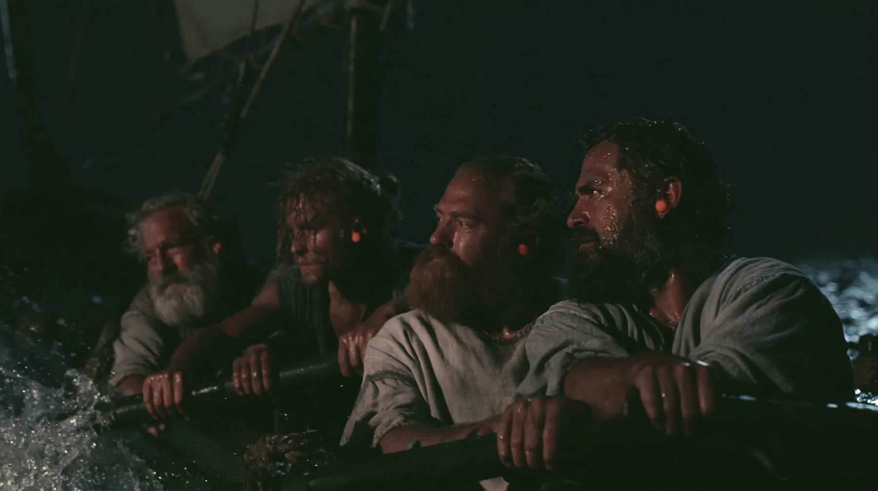 medium shot along a rowing bench of a long black ancient Greek galley with a single mast, a square sail and two banks of oars at night, four oarsmen of different ages and builds pulling their oars together, a…