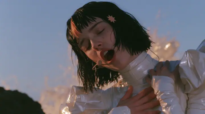 medium close-up of a Caucasian American woman in her mid-twenties with pale skin and light freckles, a glossy black blunt jaw-length bob with heavy straight bangs and one clay-orange streak through the bangs, a small…