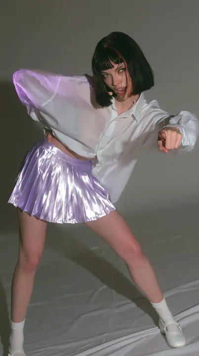 full-length photo, a Caucasian American woman in her late twenties with pale skin and a glossy black blunt bob with heavy straight bangs and one clay-orange streak, a thin headset microphone, in an oversized white…
