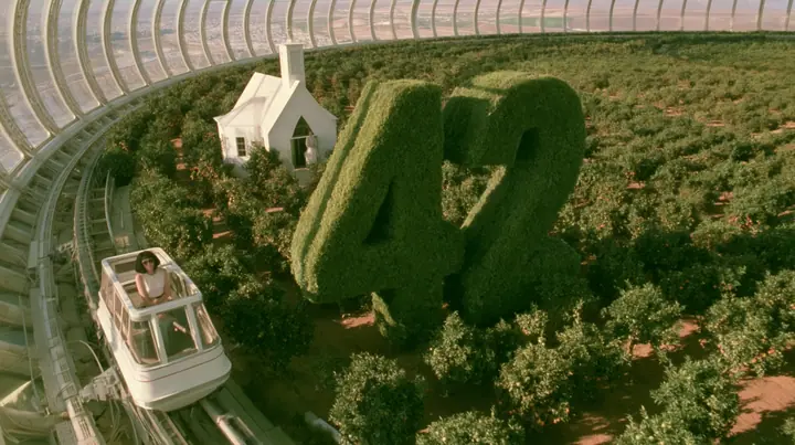Make this a 35 mm photograph from a small open white tram passing through orchards inside a space colony: beside the track a huge clipped green topiary shaped as the number 42, a small white chapel behind it. Warm…