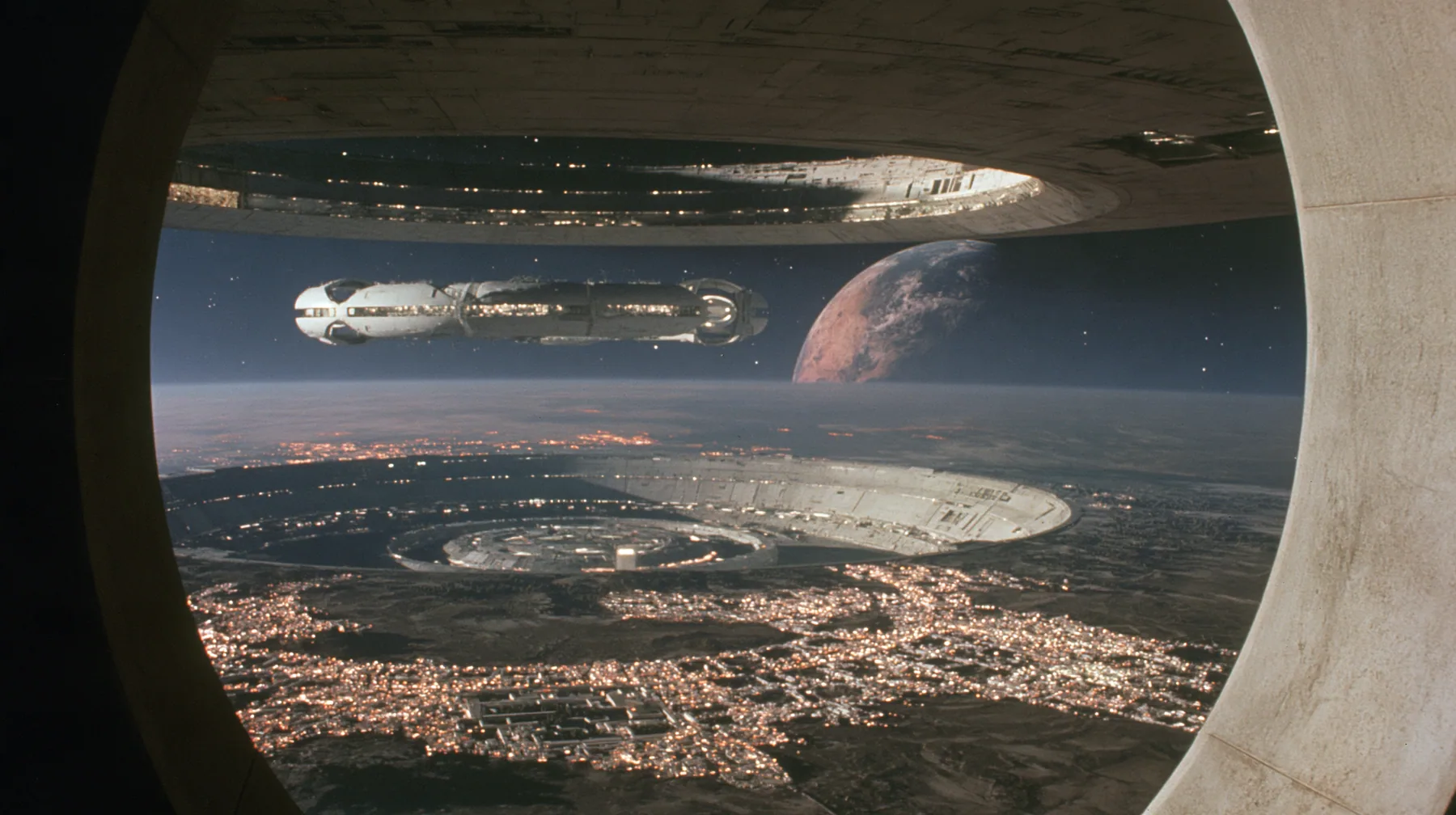 A 35 mm photograph from inside a space colony at night looking out through a vast circular end-cap window: the lit white towns curve around the dark land, and through the window the white capsule-shaped colony's…