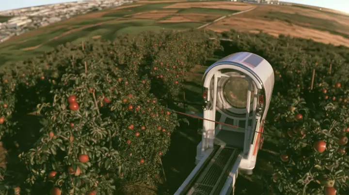 Make this the same photograph with nobody in it: remove the woman and continue the scene behind her where she stood. Keep everything else exactly: the little white tram on its rail, now empty, and the apple orchard…
