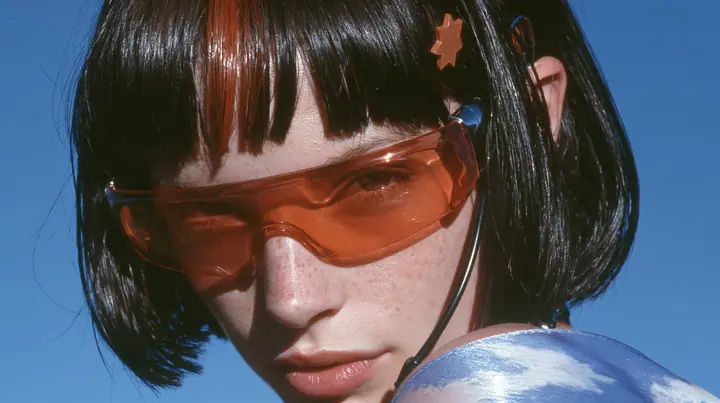 Y2K high fashion editorial, a 2001 couture magazine story: close-up of a Caucasian American woman in her mid-twenties with pale skin and light freckles, a glossy black blunt jaw-length bob with heavy straight bangs…