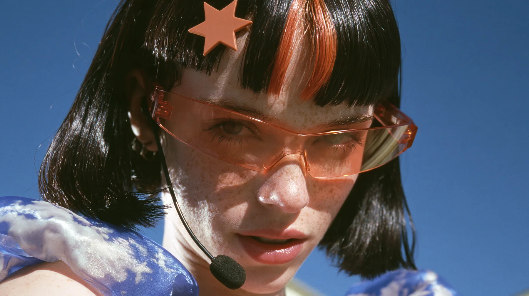 Y2K high fashion editorial, a 2001 couture magazine story: close-up of a Caucasian American woman in her mid-twenties with pale skin and light freckles, a glossy black blunt jaw-length bob with heavy straight bangs…