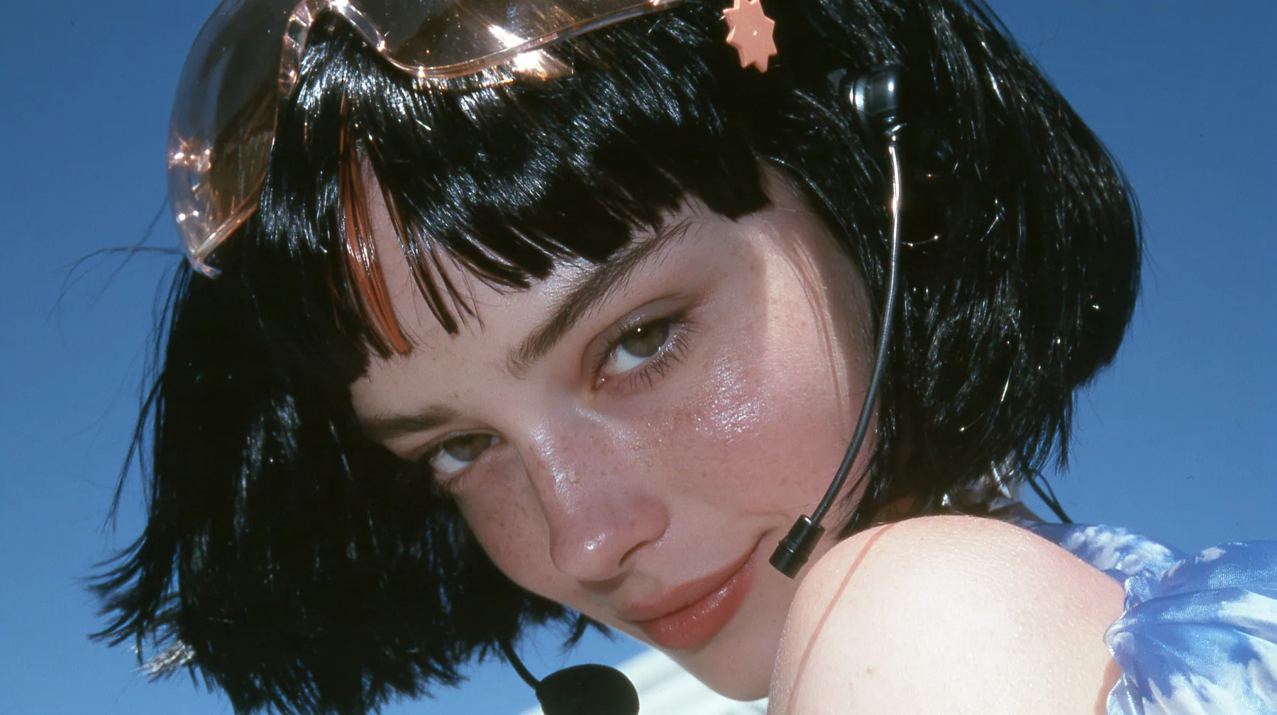 Y2K high fashion editorial, a 2001 couture magazine story: close-up of a Caucasian American woman in her mid-twenties with pale skin and light freckles, a glossy black blunt jaw-length bob with heavy straight bangs…