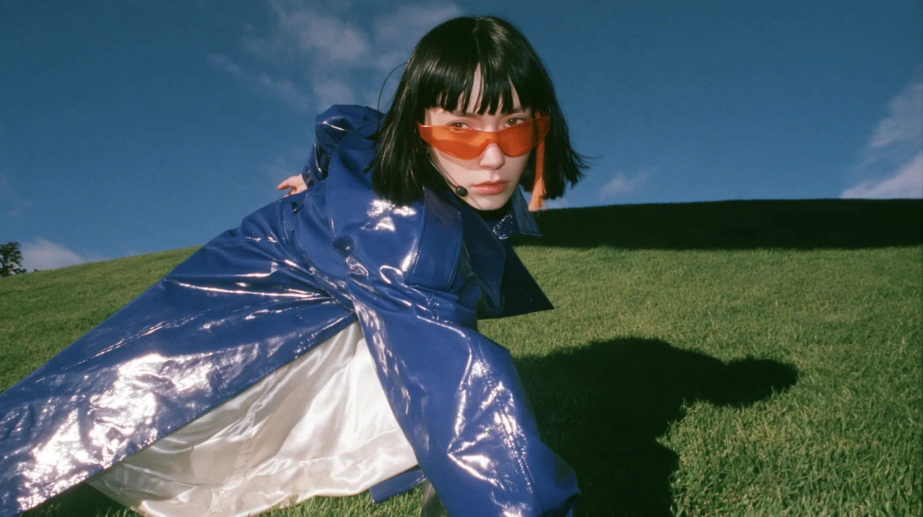 Y2K high fashion editorial, a 2001 couture magazine story: low wide shot of a young Caucasian American woman with pale skin and a glossy black blunt bob with heavy straight bangs and one clay-orange streak, a thin…