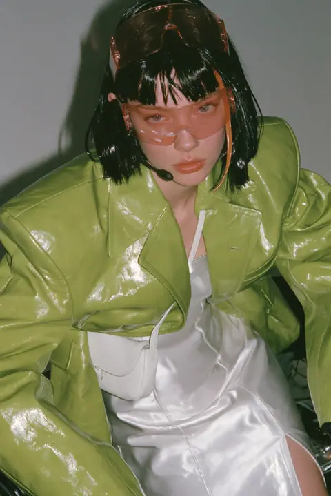 Y2K high fashion editorial, a 2001 couture magazine story: full-length shot, head to toe with the feet in frame, of a young Caucasian American woman with pale skin and a glossy black blunt bob with heavy straight…