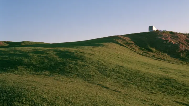 Y2K high fashion editorial photograph, 2001: a smooth rolling bright-green grassy hill with soft curves, the grass short and velvety at dusk, a dark translucent CRT monitor and a person lying in the grass beside it…