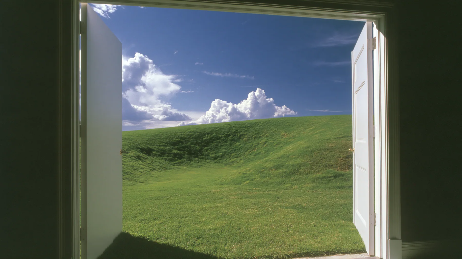 Y2K high fashion editorial photograph, 2001: first-person view stepping out of a white door onto a sunny manicured lawn, a smooth rolling bright-green grassy hill with soft curves, the grass short and velvety rising…