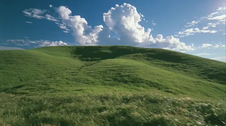 Y2K high fashion editorial photograph, 2001: first-person view walking up a smooth rolling bright-green grassy hill with soft curves, the grass short and velvety, the grass rushing past at the bottom of frame, the…