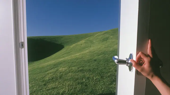 Y2K high fashion editorial photograph, 2001: first-person view of a hand on the chrome handle of a tall white door swinging open onto a bright morning, a smooth rolling bright-green grassy hill with soft curves, the…