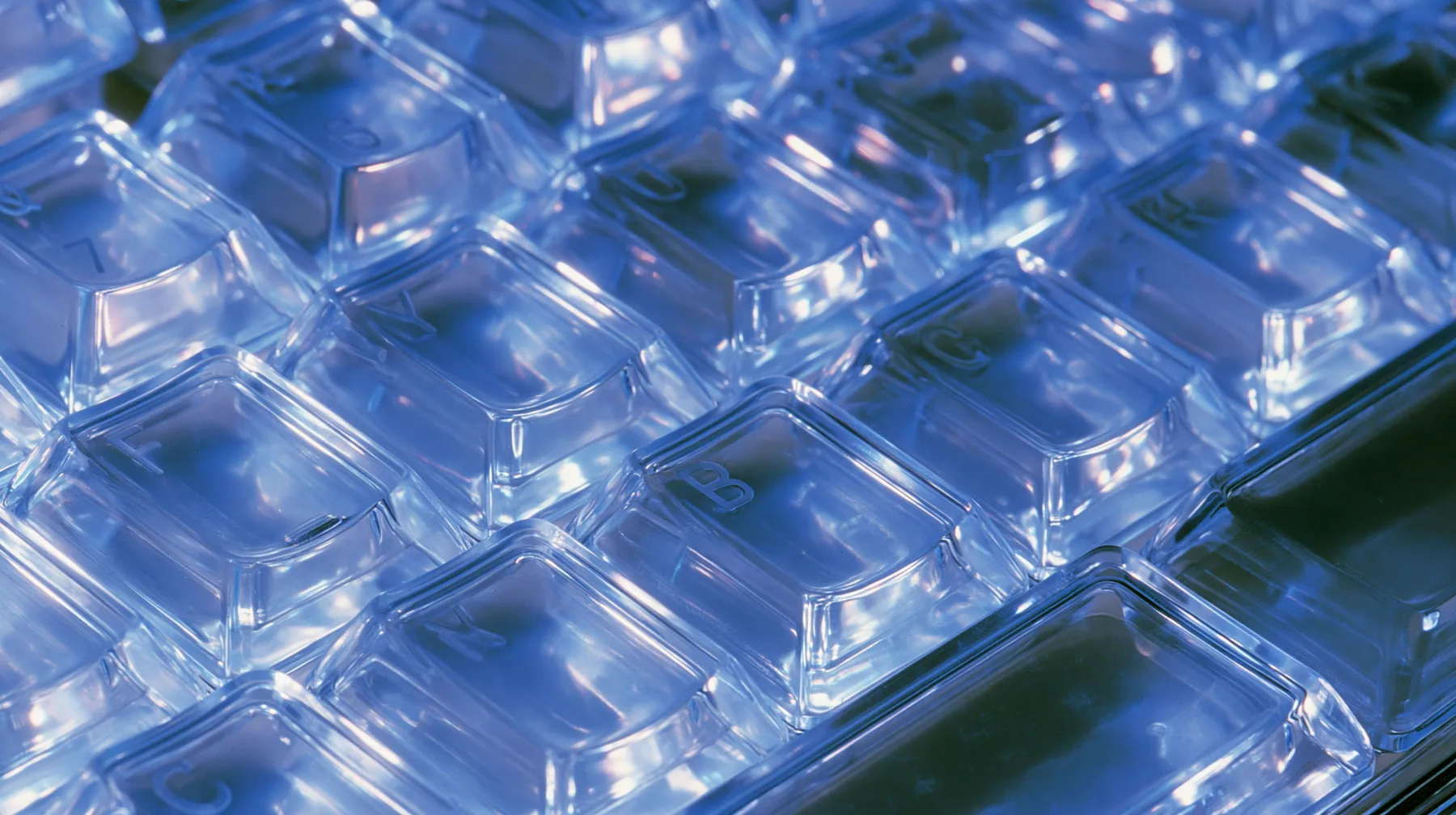 Y2K high fashion editorial photograph, 2001: a luxury product macro of a translucent ice-blue keyboard from 2001, its keys glowing softly, shallow depth of field, no text, no letters, no logos