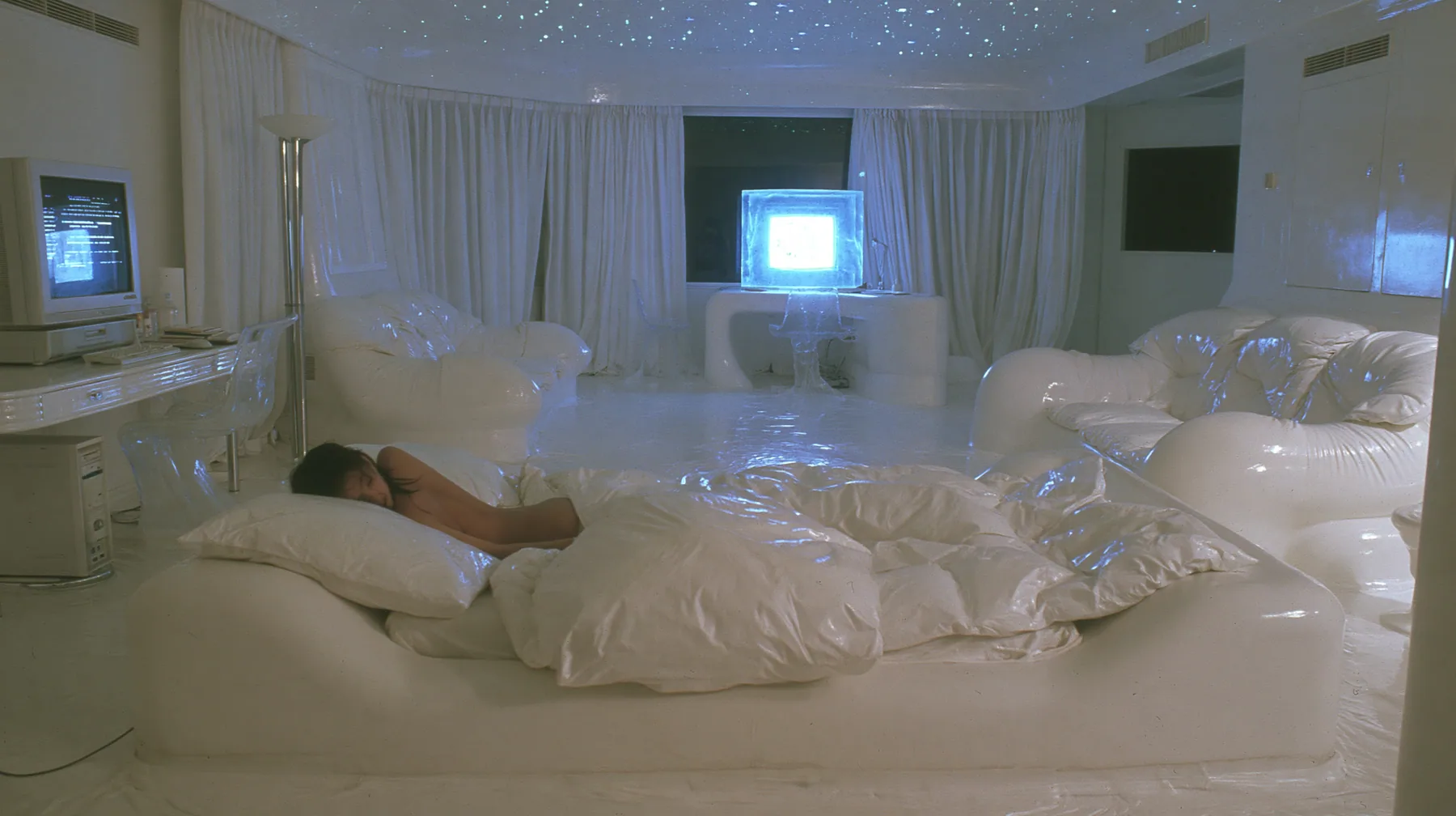 Y2K high fashion editorial photograph, 2001: first-person view from the pillow of a white low bed in a 2001 high-fashion minimalist white loft apartment with molded white plastic furniture, a white lacquer desk,…
