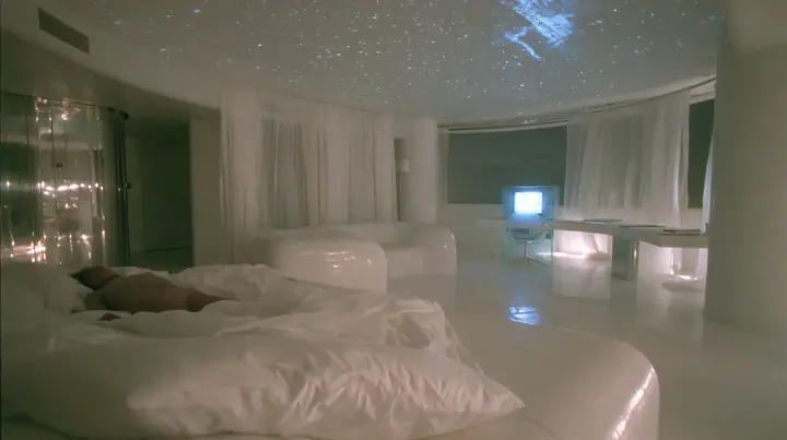 Y2K high fashion editorial photograph, 2001: first-person view from the pillow of a white low bed in a 2001 high-fashion minimalist white loft apartment with molded white plastic furniture, a white lacquer desk,…