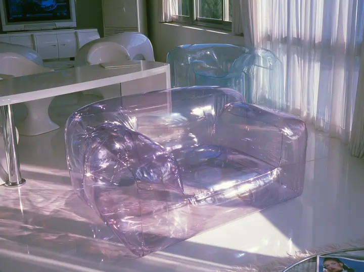 Y2K high fashion editorial photograph, 2001: a translucent violet inflatable armchair in a 2001 high-fashion minimalist white loft apartment with molded white plastic furniture, a white lacquer desk, chrome and…