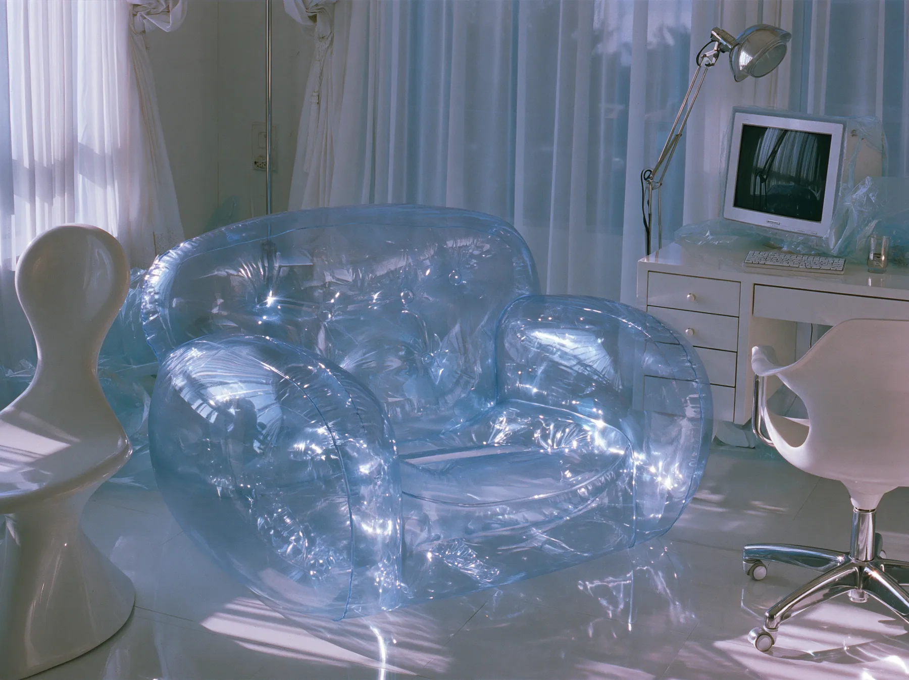 Y2K high fashion editorial photograph, 2001: a translucent violet inflatable armchair in a 2001 high-fashion minimalist white loft apartment with molded white plastic furniture, a white lacquer desk, chrome and…