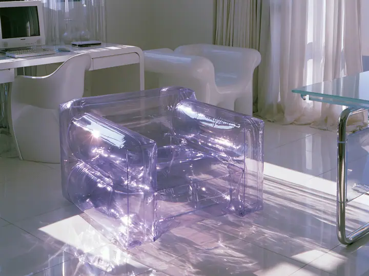 Y2K high fashion editorial photograph, 2001: a translucent violet inflatable armchair in a 2001 high-fashion minimalist white loft apartment with molded white plastic furniture, a white lacquer desk, chrome and…