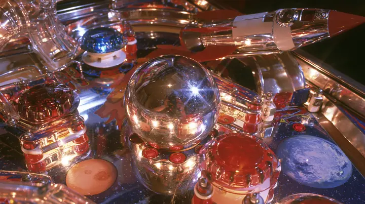 Y2K high fashion editorial photograph, 2001: a luxury product photograph of a glossy chrome and candy-colored space-themed pinball table, a shiny silver ball, glowing bumpers, a rocket ramp and planets, no text, no…