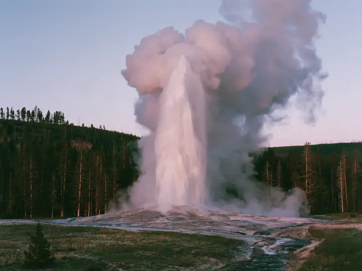 Y2K high fashion editorial photograph, 2001: a luxury travel campaign photograph of a tall geyser erupting at dawn against a pale pink sky, steam billowing, lodgepole pines behind, no text, no letters, no logos