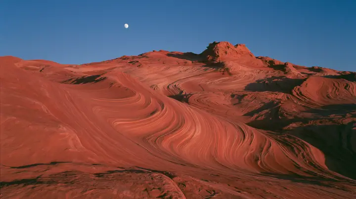 Y2K high fashion editorial photograph, 2001: a luxury campaign landscape of red sandstone dunes under a deep blue dusk sky with a pale full moon, medium-format slide film, no text, no letters, no logos
