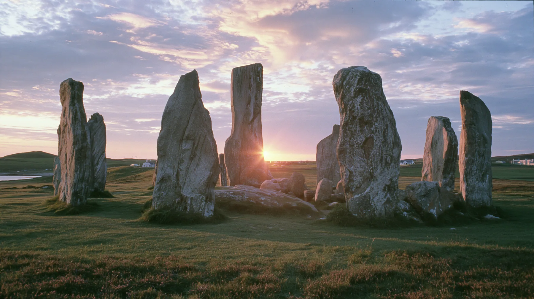 Y2K high fashion editorial photograph, 2001: a luxury campaign landscape of ancient standing stones silhouetted against a glowing violet and amber sunset, medium-format slide film, no text, no letters, no logos