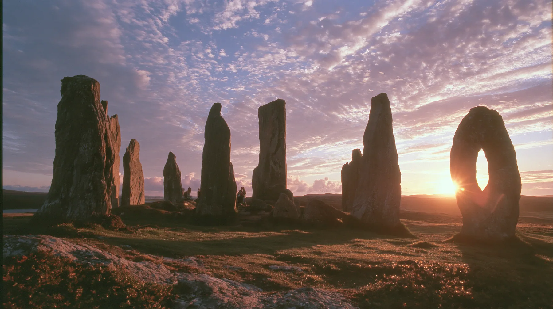 Y2K high fashion editorial photograph, 2001: a luxury campaign landscape of ancient standing stones silhouetted against a glowing violet and amber sunset, medium-format slide film, no text, no letters, no logos