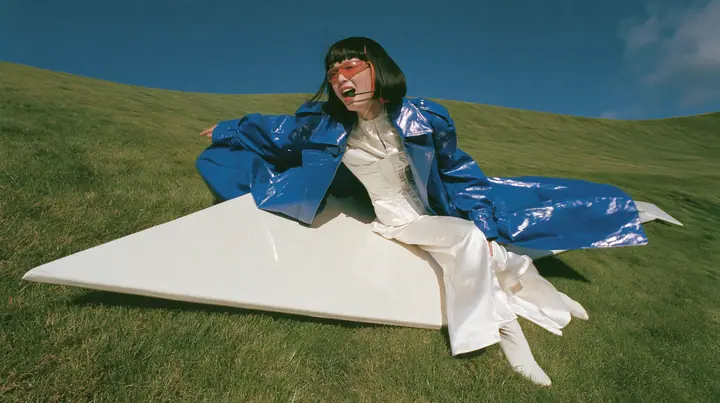 Y2K high fashion editorial, a 2001 couture magazine story: a wide shot of a young Caucasian American woman with pale skin and a glossy black blunt bob with heavy straight bangs and one clay-orange streak, a thin…