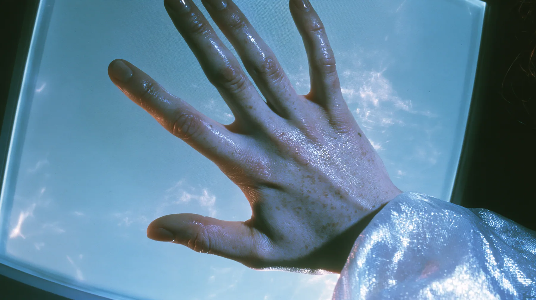 Y2K high fashion editorial, a 2001 couture magazine story: a close-up of a pale freckled palm and fingertips pressed flat against the inside of a glowing translucent CRT screen glass, seen from outside the screen in…
